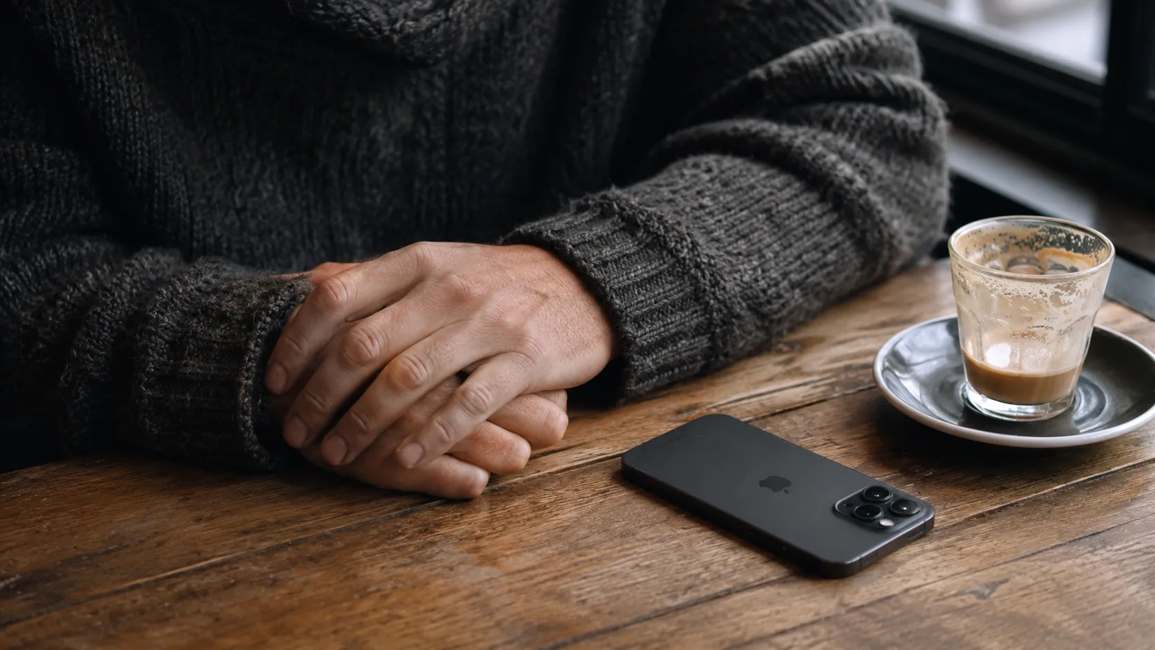 A person sitting at a cafe table with a smartphone resting face down, representing a pause in online dating.
